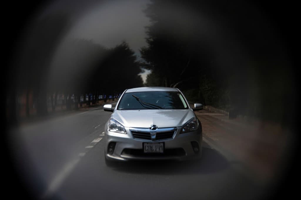 View from inside a car on a road through a narrow circular field of vision, with dark blurred edges — illustrating advanced glaucoma tunnel vision